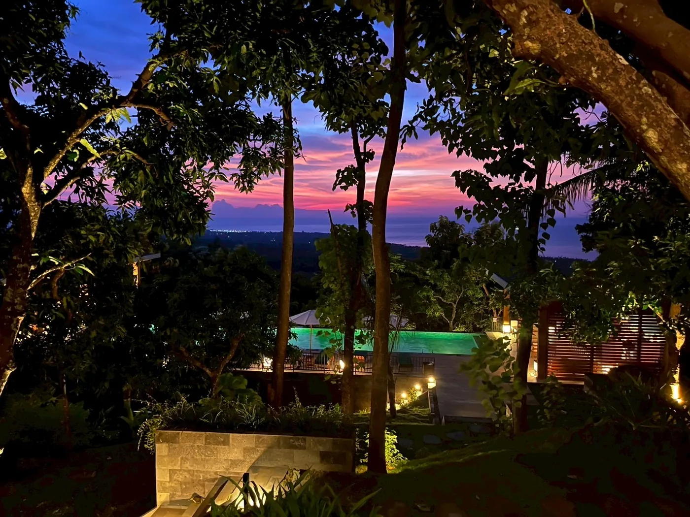 An eco-resort at dusk, with a pool and warm lights among the trees